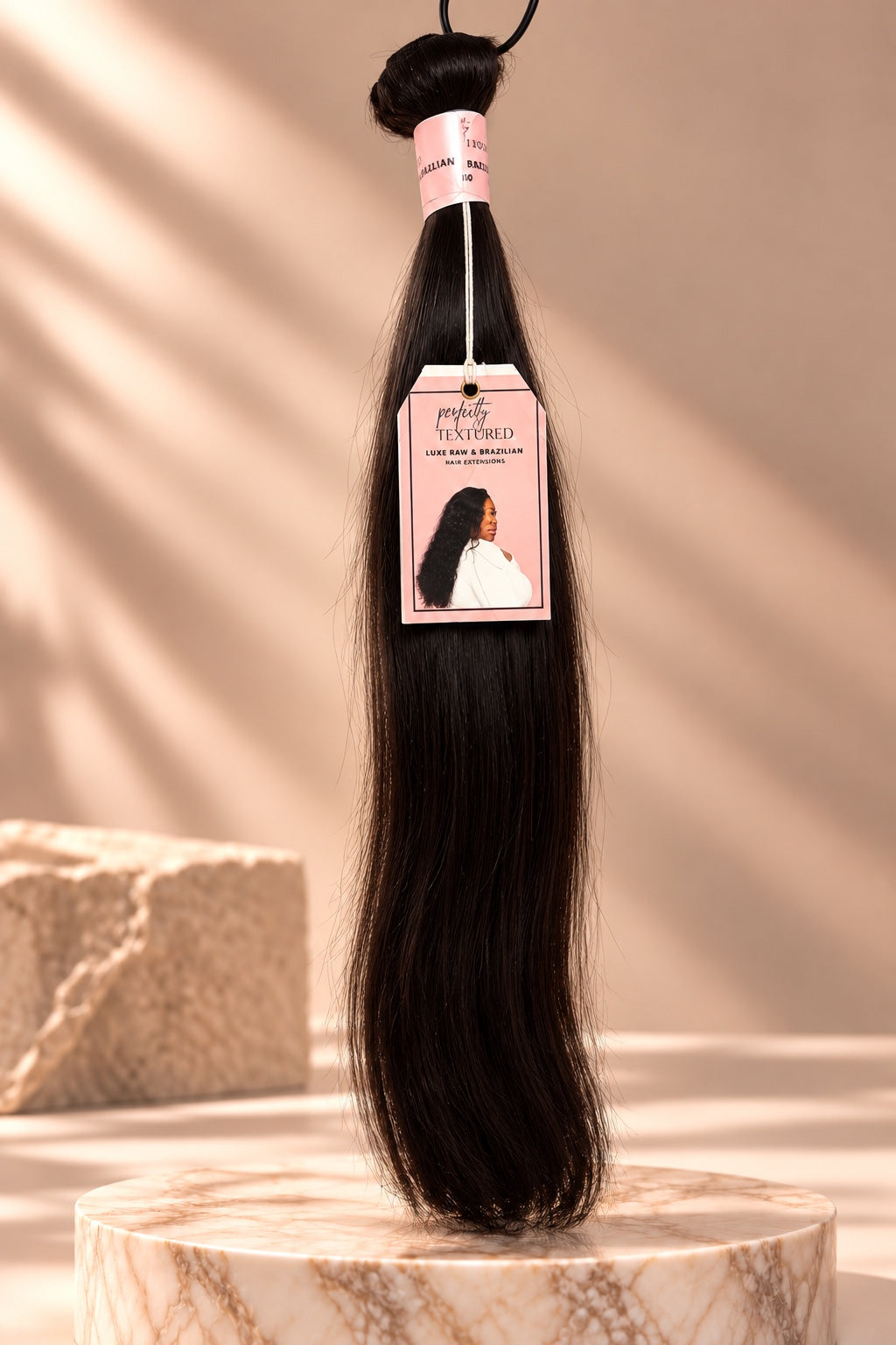 Perfectly Textured Smooth and Straight dark straight hair extension bundle with pink brand tag on marble pedestal